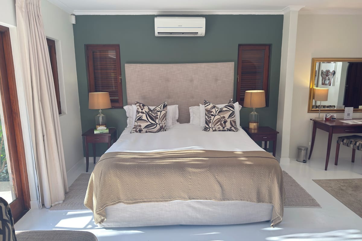 Une chambre d’hôtel avec un grand lit, deux tables de chevet avec des lampes, un climatiseur fixé au mur et une fenêtre avec des rideaux.
