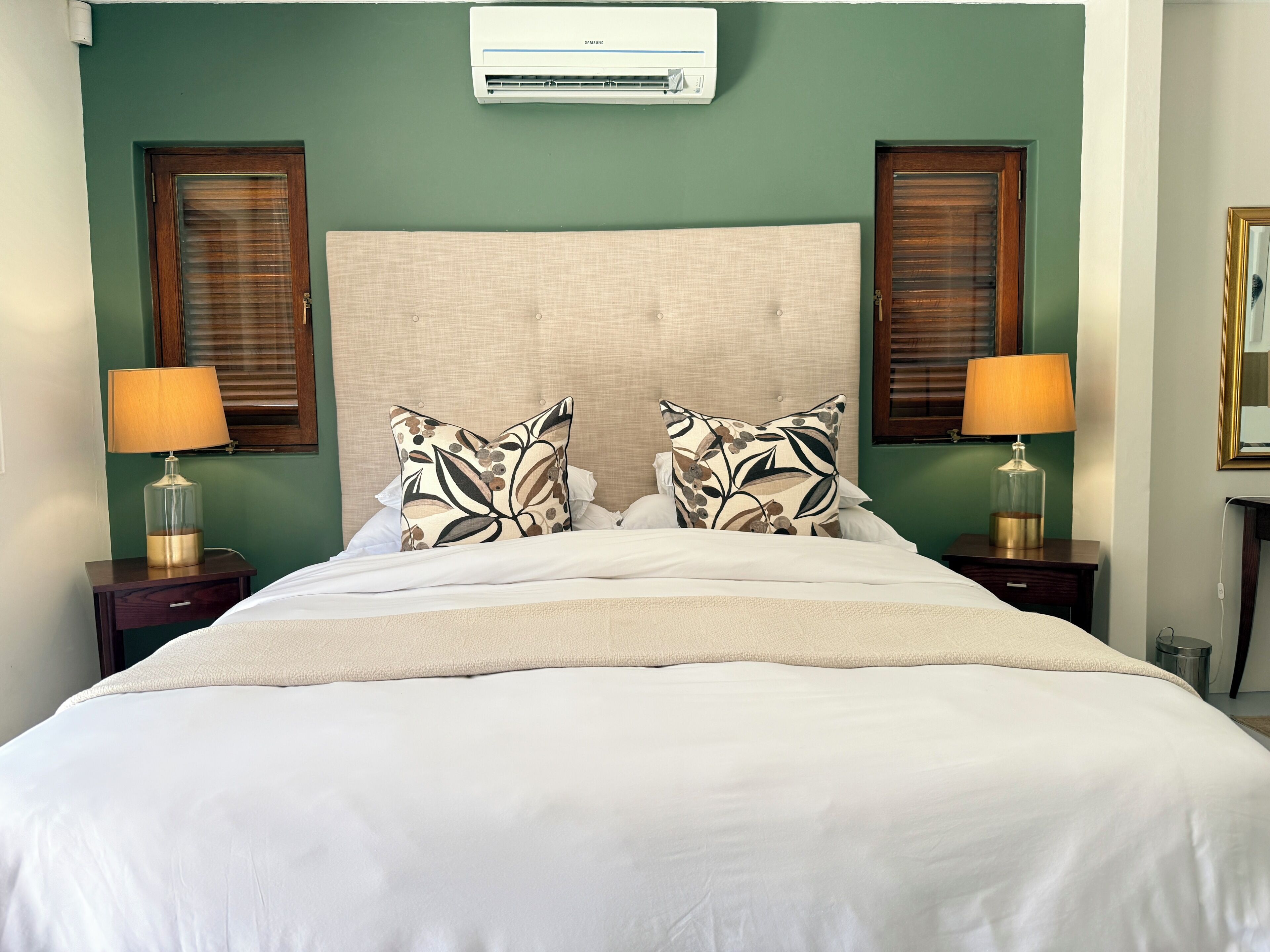 Habitación de hotel con cama, dos mesitas de noche, lámparas, equipo de aire acondicionado y ventana con persianas.