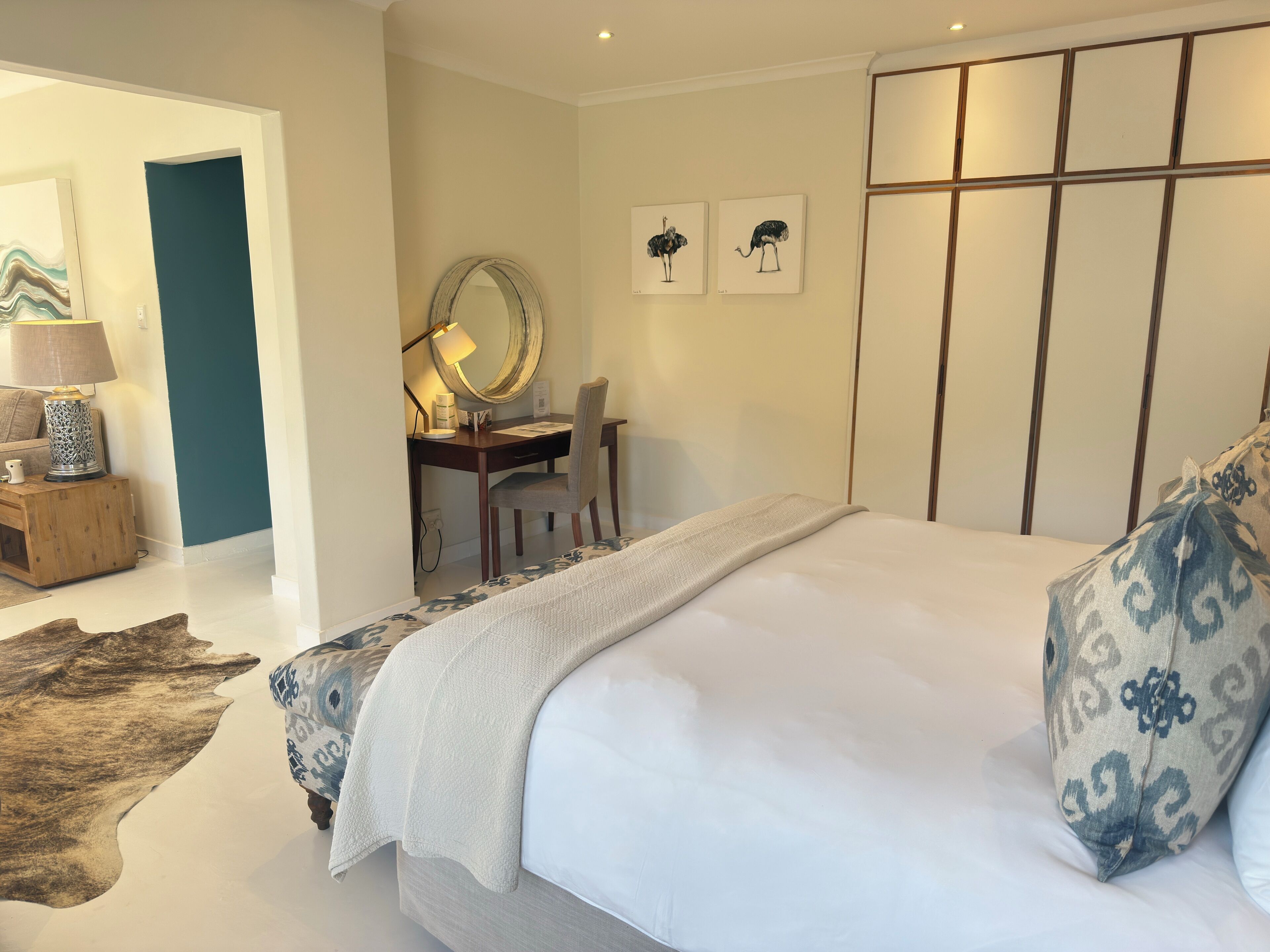 Un dormitorio con una cama grande, un escritorio con silla, un espejo y obras de arte en la pared.