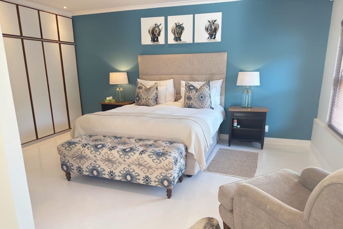 Une chambre à coucher avec un grand lit, des tables de chevet, une chaise et des œuvres d’art accrochées au mur.
