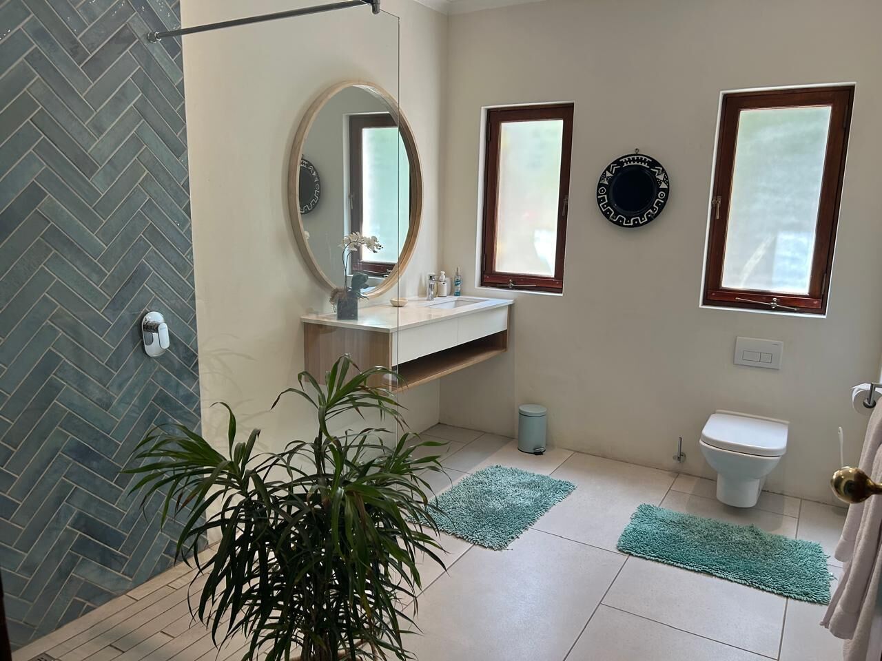 A bathroom with a herringbone tile floor, a sink with a mirror, a toilet, and a potted plant.