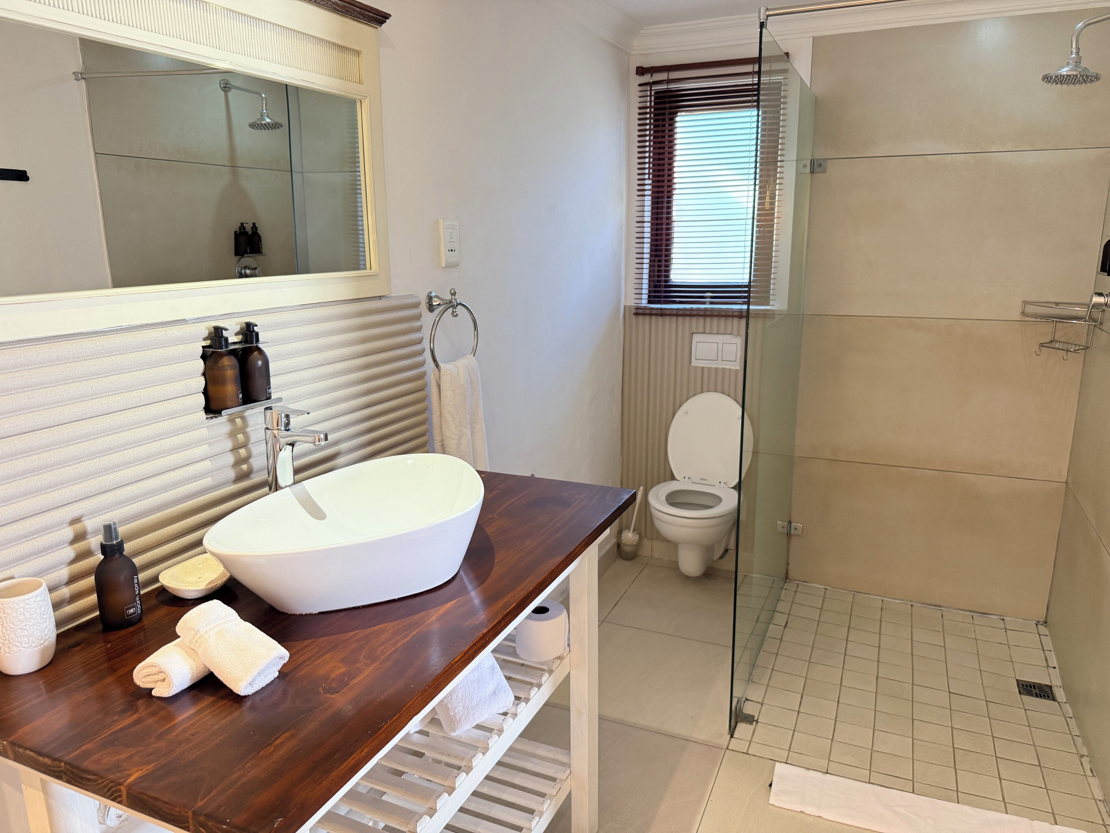 Een badkamer met een houten wastafelmeubel, een witte wastafel, een douchecabine met glazen wanden en een toilet.