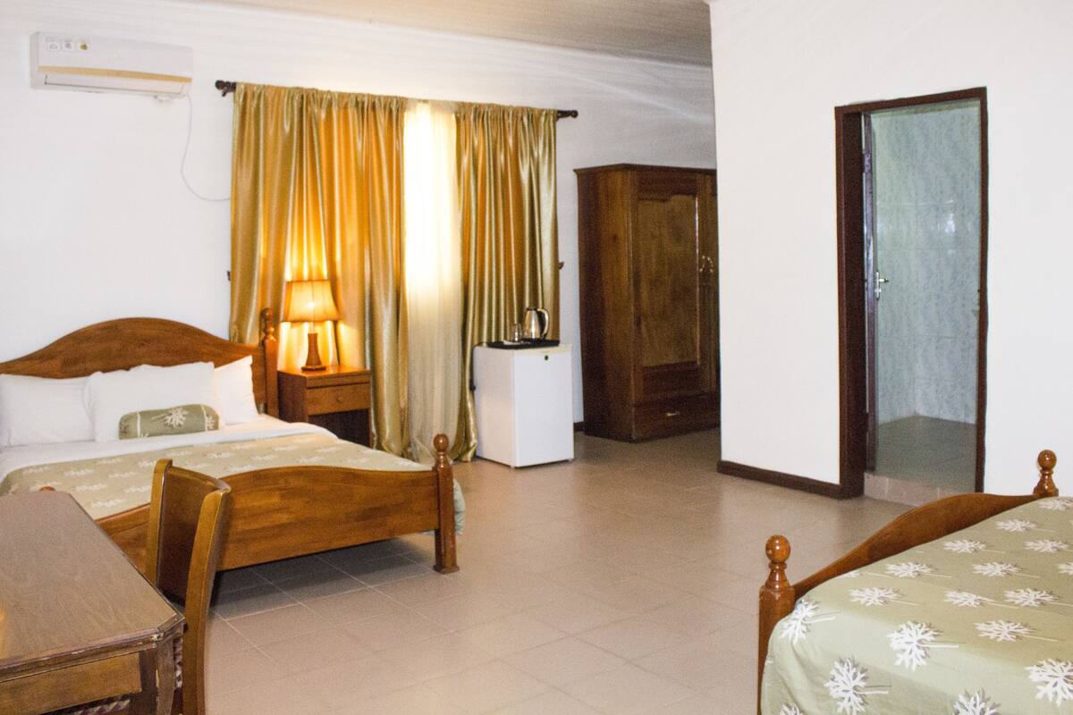 A hotel room with a wooden bed, a bedside table, a lamp, a wardrobe, and a mirror.
