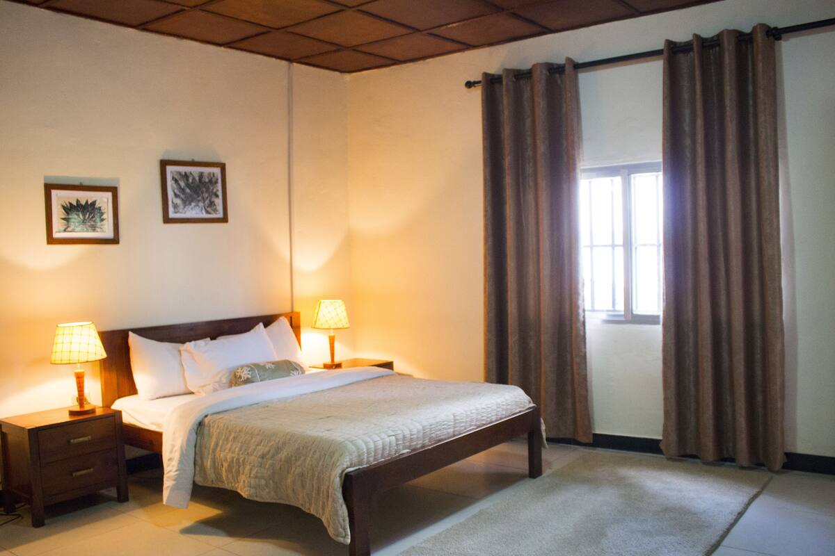A neatly arranged bedroom with a large bed, two bedside tables with lamps, and a window with curtains.