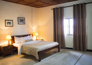 Un dormitorio ordenado con una cama grande, dos mesitas de noche con lámparas y una ventana con cortinas.