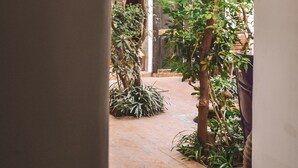 An arched corridor with a tiled floor, leading to a garden area with potted plants and a wooden door. - Riad Houdou (Marrakech)