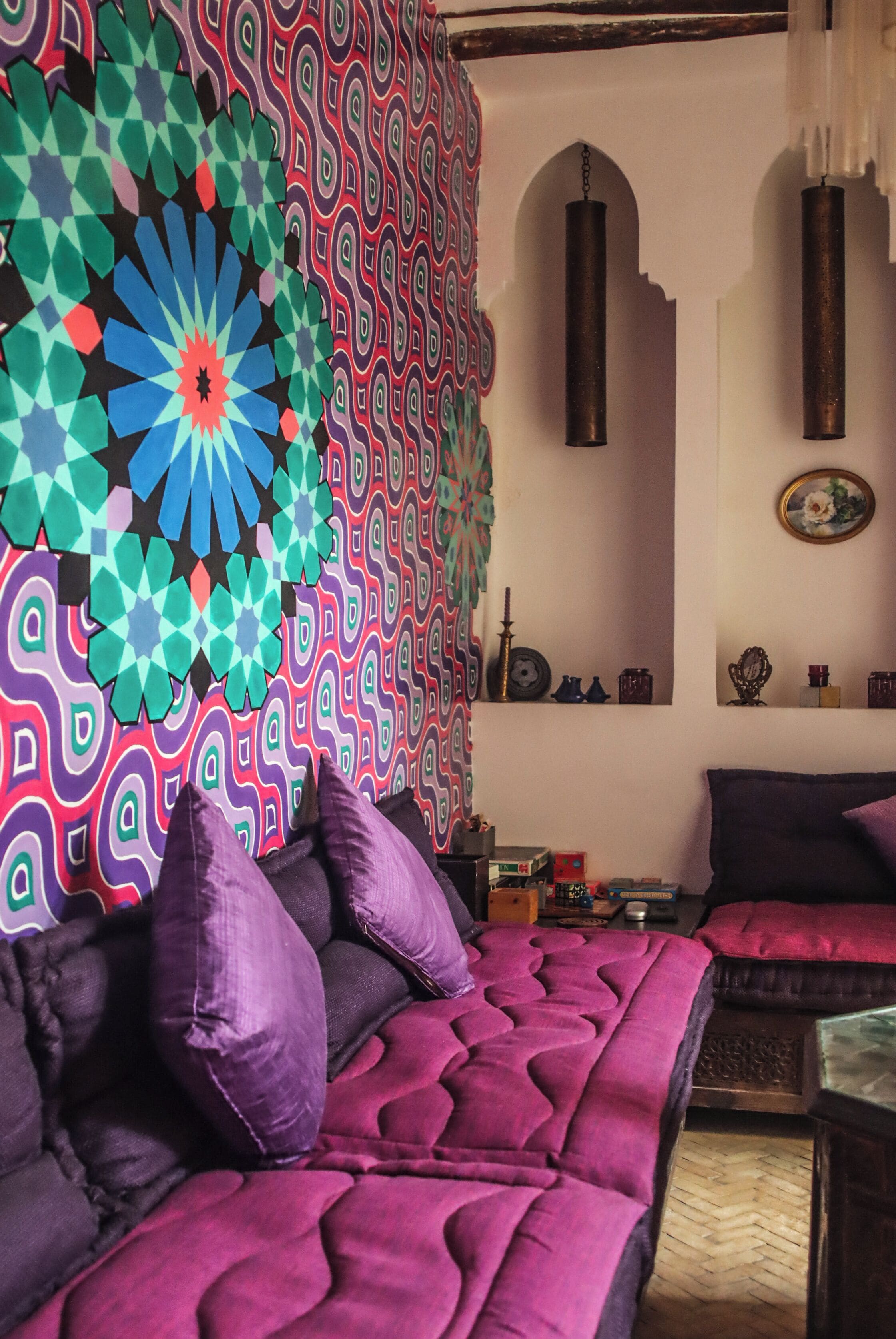 A room with a patterned tapestry, a bed with purple bedding, and a wooden floor.