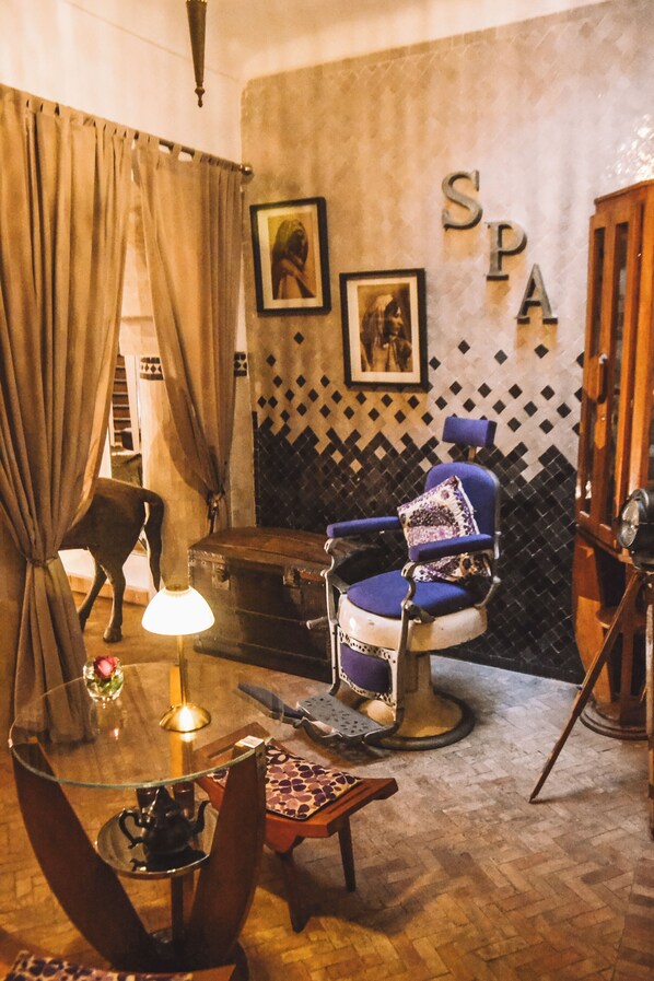 A room with a vintage chair, a small table with a lamp, a suitcase, and a wall with 'SPA' letters.