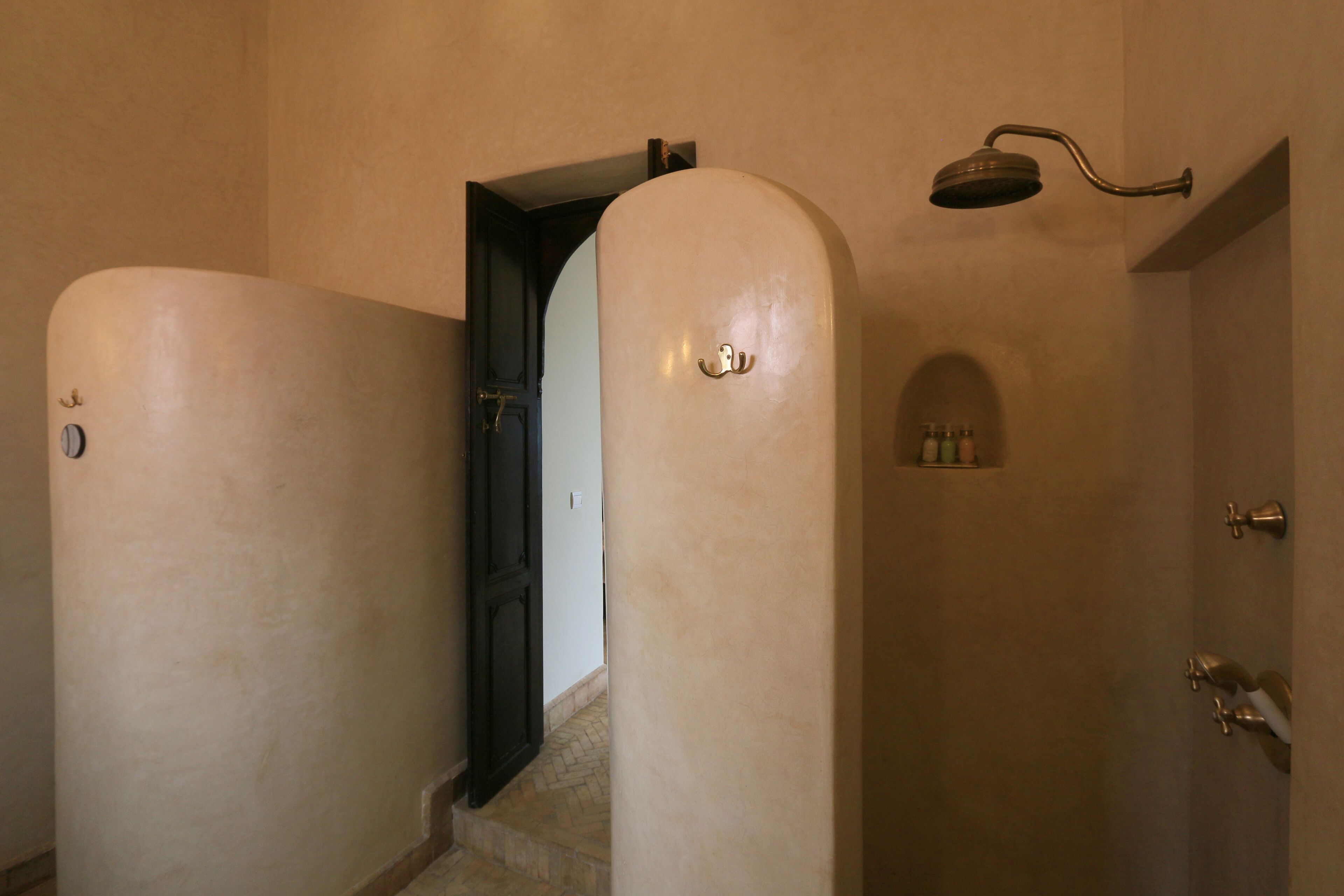 Un couloir avec un espace douche, comprenant un pommeau de douche et une étagère pour les articles de toilette.