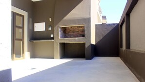 A narrow outdoor corridor with a concrete floor, a door on the left, and a brick fireplace on the right. - Discovery Riverlets Apartment (Windhoek)