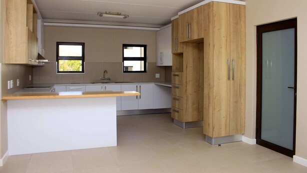 A modern kitchen with white cabinets, a wooden island, and a sliding glass door. - Discovery Riverlets Apartment (Windhoek)