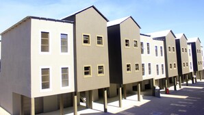 A row of modern, multi-story buildings with uniform architecture, featuring a series of windows and a flat roof. - Discovery Riverlets Apartment (Windhoek)