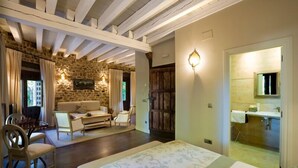 A room with a stone wall, wooden beams, a sofa, a dining table, and a bed. - El Morendal (Almarza)