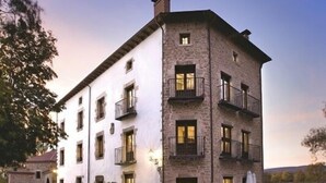 A multi-story building with a stone facade, multiple balconies, and a courtyard with outdoor seating. - El Morendal (Almarza)
