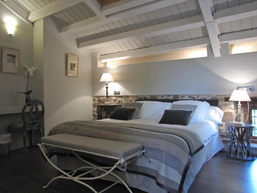 Een slaapkamer met een bed, bedlampjes, een klein tafeltje en een stoel.