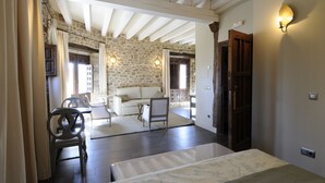 A room with a stone wall, wooden beams, a white sofa, a dining table, and a bed. - El Morendal (Almarza)