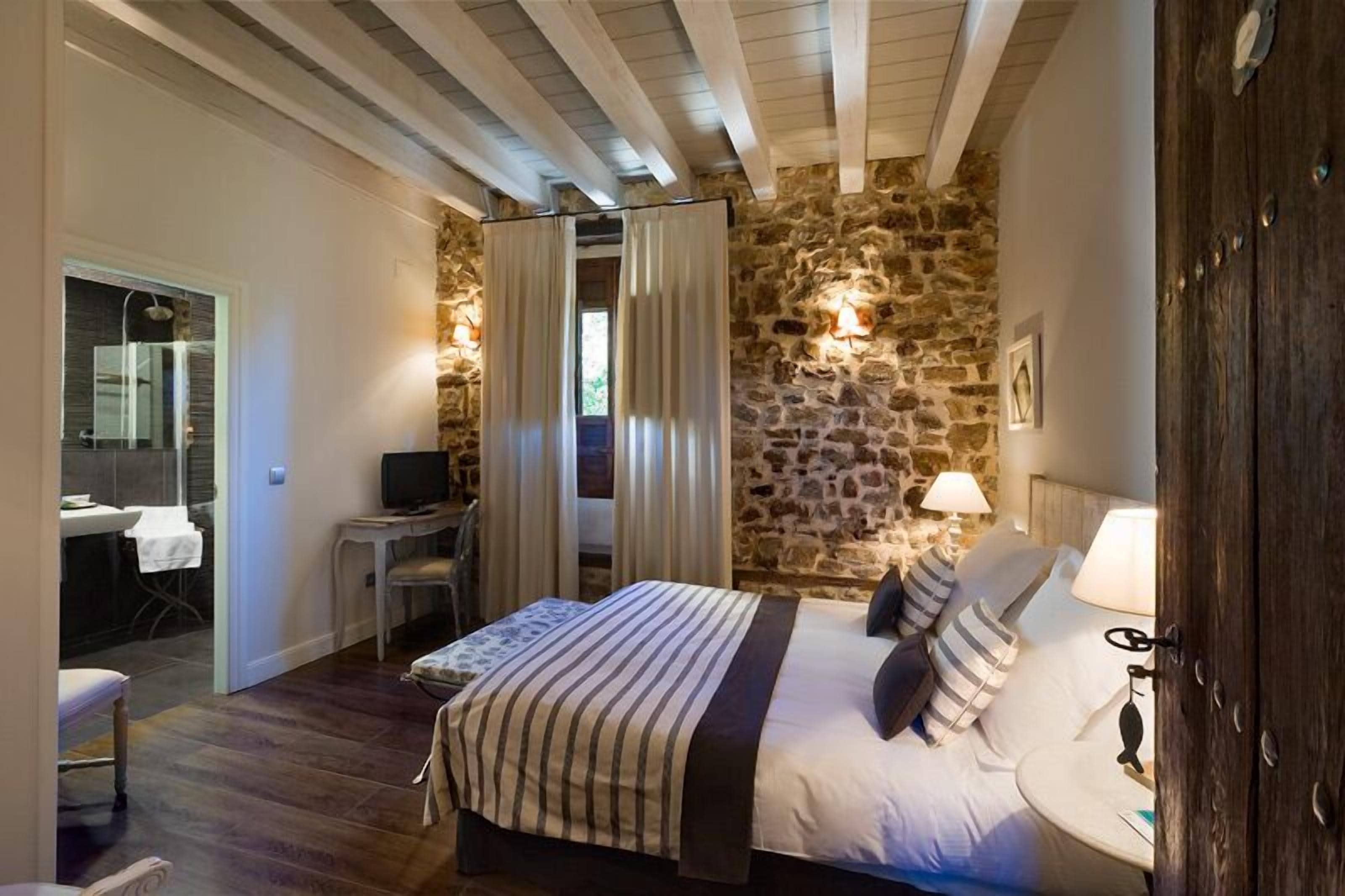 Un dormitorio con pared de piedra, una cama con ropa de cama a rayas, un escritorio con silla y un televisor.