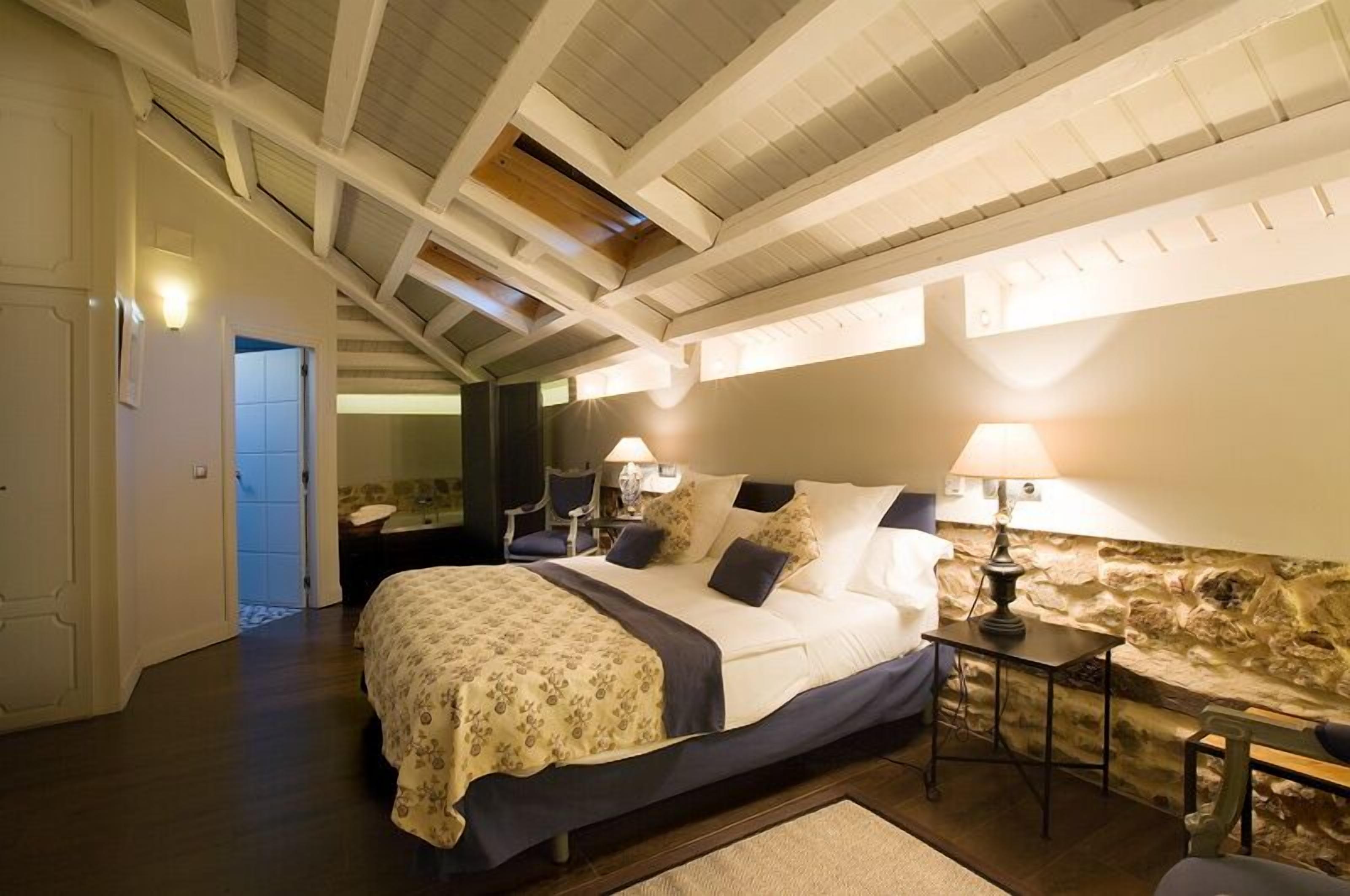 Un dormitorio con cama, mesita de noche, lámpara y pared de piedra.