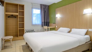 A hotel room with a large bed, a wooden wardrobe, a small table, and a chair. - B&B HOTEL Nîmes Ville Active (Nîmes)