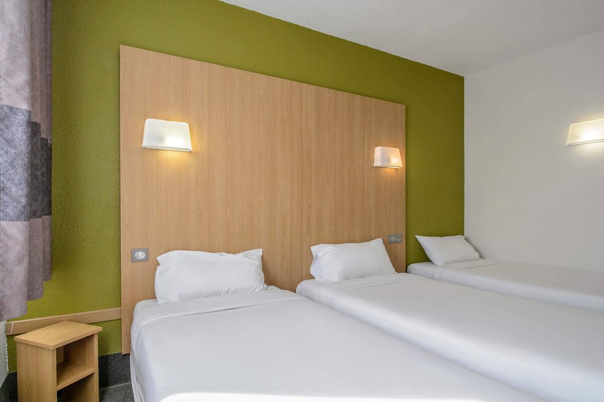 A hotel room with two beds, a wooden headboard, and two wall-mounted lights.