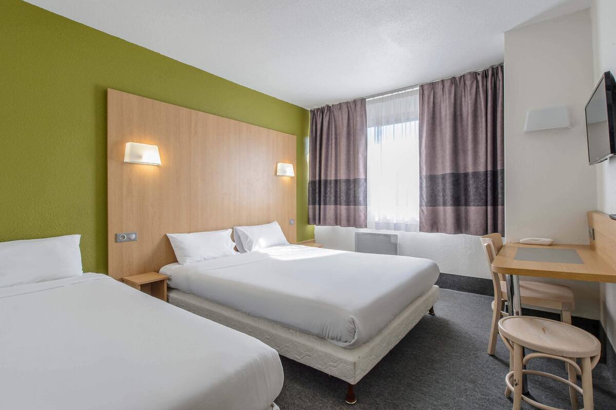 A hotel room with two beds, a desk, and a chair.