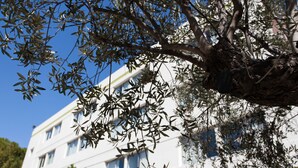 A building with multiple windows and a tree in front. - B&B HOTEL Nîmes Ville Active (Nîmes)