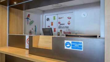 A reception desk with a wooden counter and a metal desk. There is a wall with a clock and various colorful stickers.