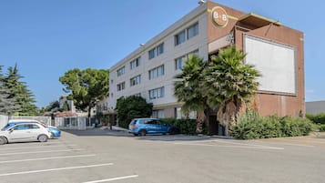Een hotel met een moderne gevel, een parkeerplaats en twee daar geparkeerde auto's.