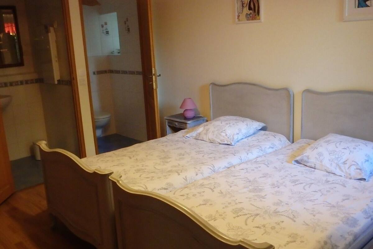 Een slaapkamer met een bed, nachtkastje, spiegel en een deur naar een badkamer.