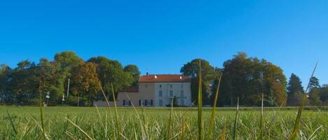 A large house with a red roof, surrounded by a grassy field and trees.