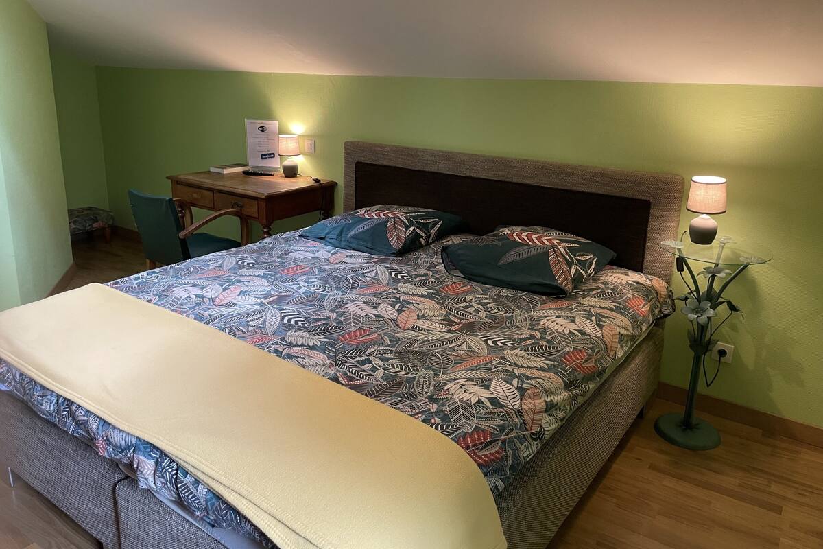 Een slaapkamer met een bed, een bureau, een stoel en een lamp.
