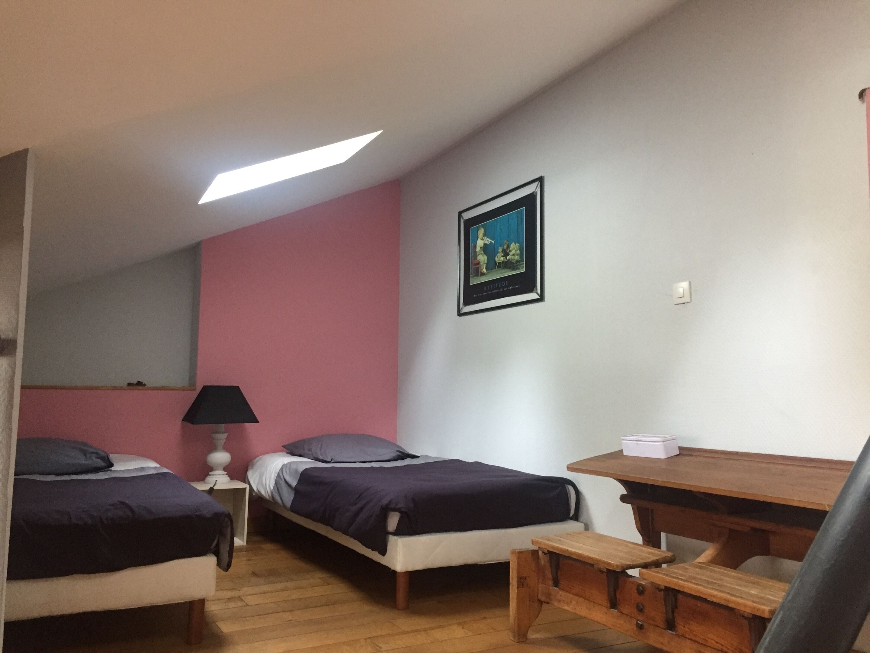 Una habitación con dos camas, un escritorio, una silla, una lámpara y un cuadro en la pared.