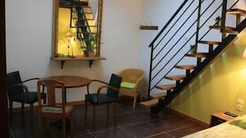 Ein Zimmer mit einem Bett, einem Esstisch mit Stühlen, einer Treppe und einem Spiegel.