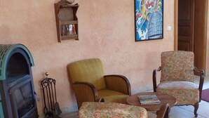 Un salón con chimenea, dos sillones estampados, una mesita con una revista y un cuadro en la pared.