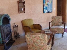 A living room with a fireplace, two floral armchairs, a small table with a magazine, and a painting on the wall.