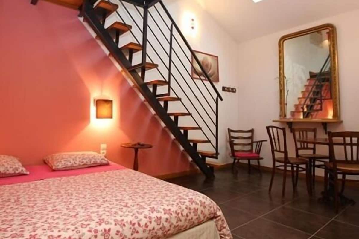 Een slaapkamer met een bed, een bureau, een stoel, een spiegel en een trap.