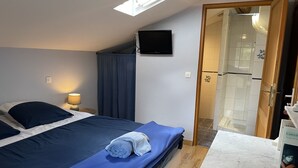 Un dormitorio con cama, televisión montada en la pared, baño visible a través de una puerta abierta y encimera de mármol.
