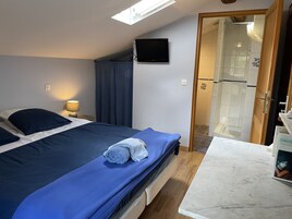 A bedroom with a bed, a TV mounted on the wall, a bathroom visible through an open door, and a marble countertop.
