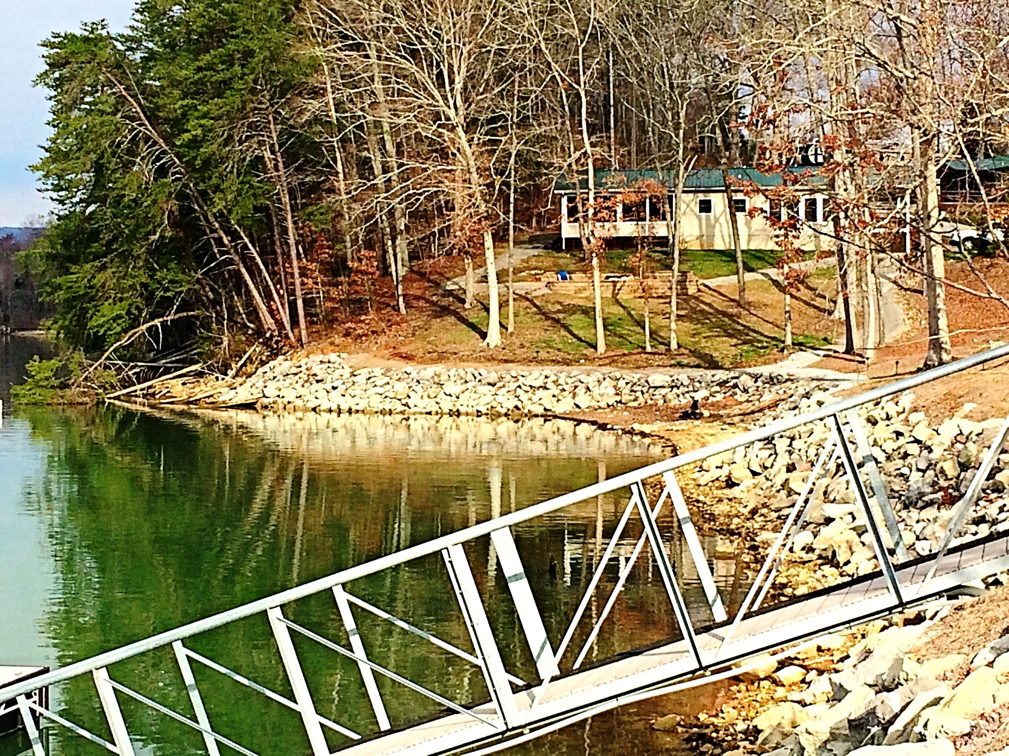 Una propiedad frente al lago con muelle, pared de piedra y una casa con techo verde.