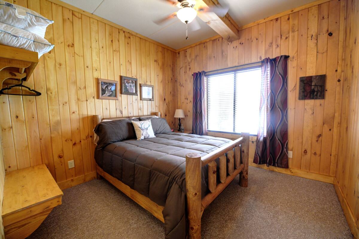 Ein Schlafzimmer mit Holzvertäfelung, einem Bett, einem Deckenventilator und einem Fenster mit Vorhängen.