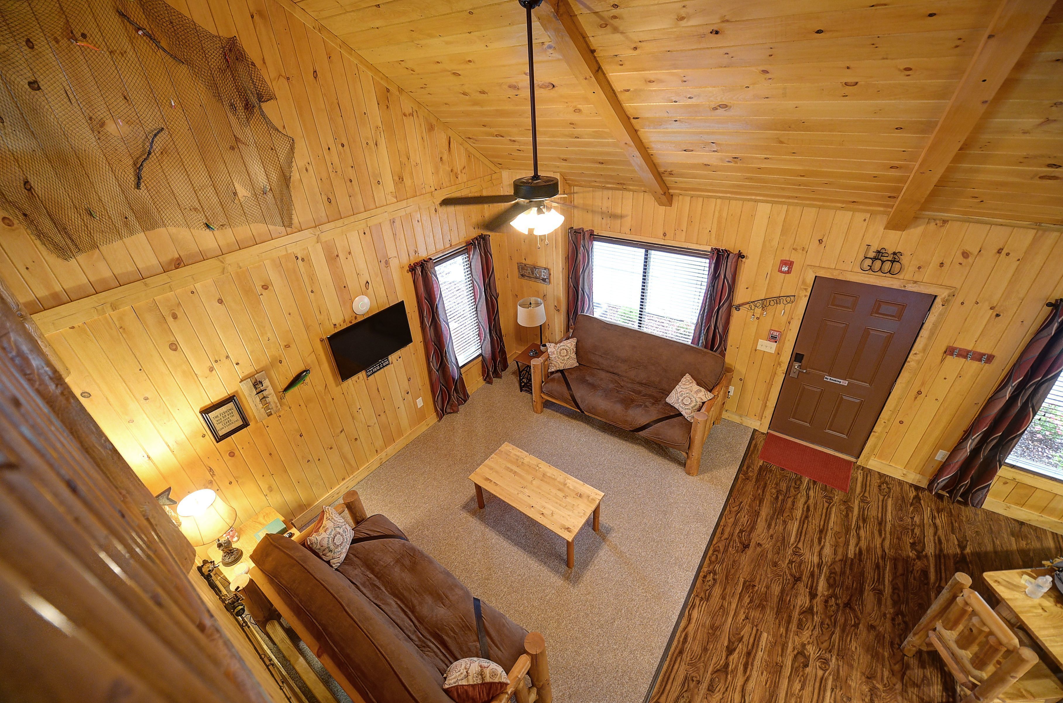 Interior de una cabaña de madera con un sofá, una mesa de madera y un ventilador de techo.