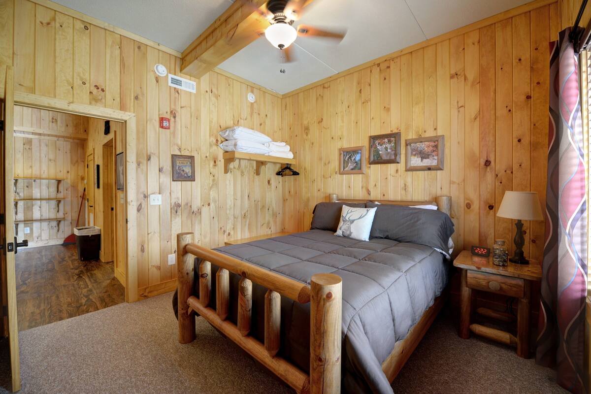Ein Zimmer mit Holzwänden, einem Bett, einem Nachttisch und einem Deckenventilator.