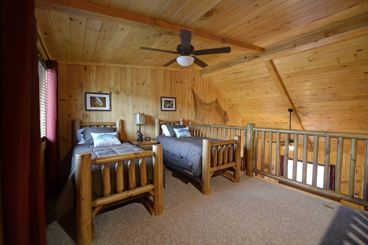 Eine Holzhütte mit zwei Betten, einem Deckenventilator und Holzwänden.