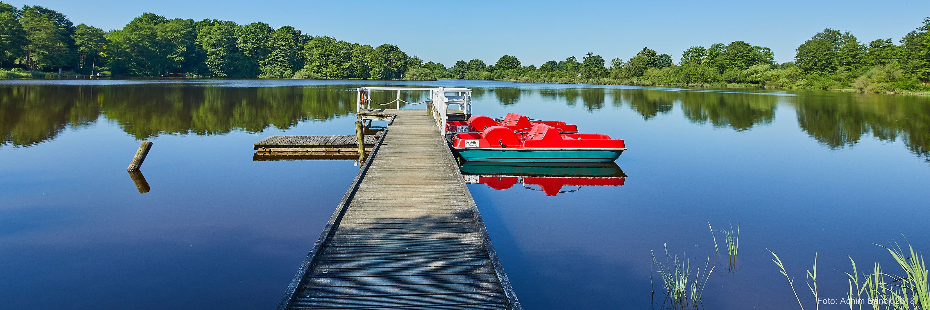 Een houten steiger die zich uitstrekt over kalm water, met een rode boot aan het einde afgemeerd.