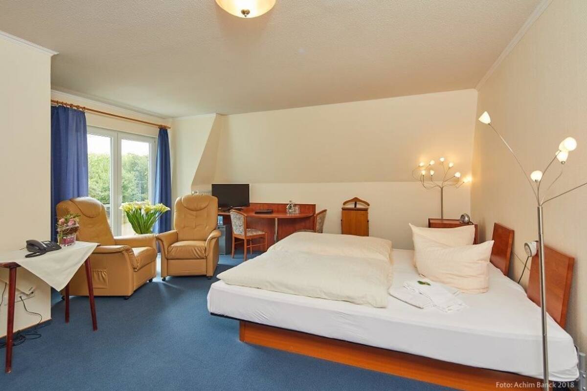 A hotel room with a bed, two chairs, a desk, and a TV.