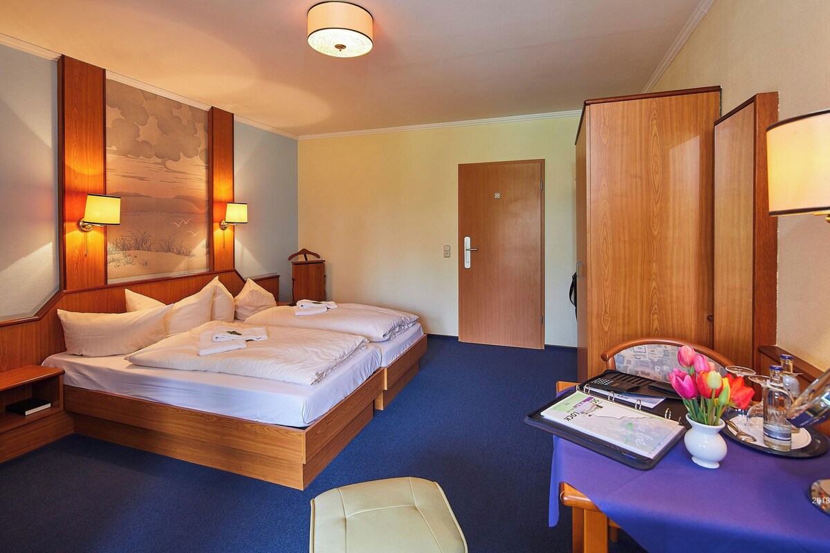 A hotel room with a double bed, a desk with a computer, a chair, and a wardrobe.
