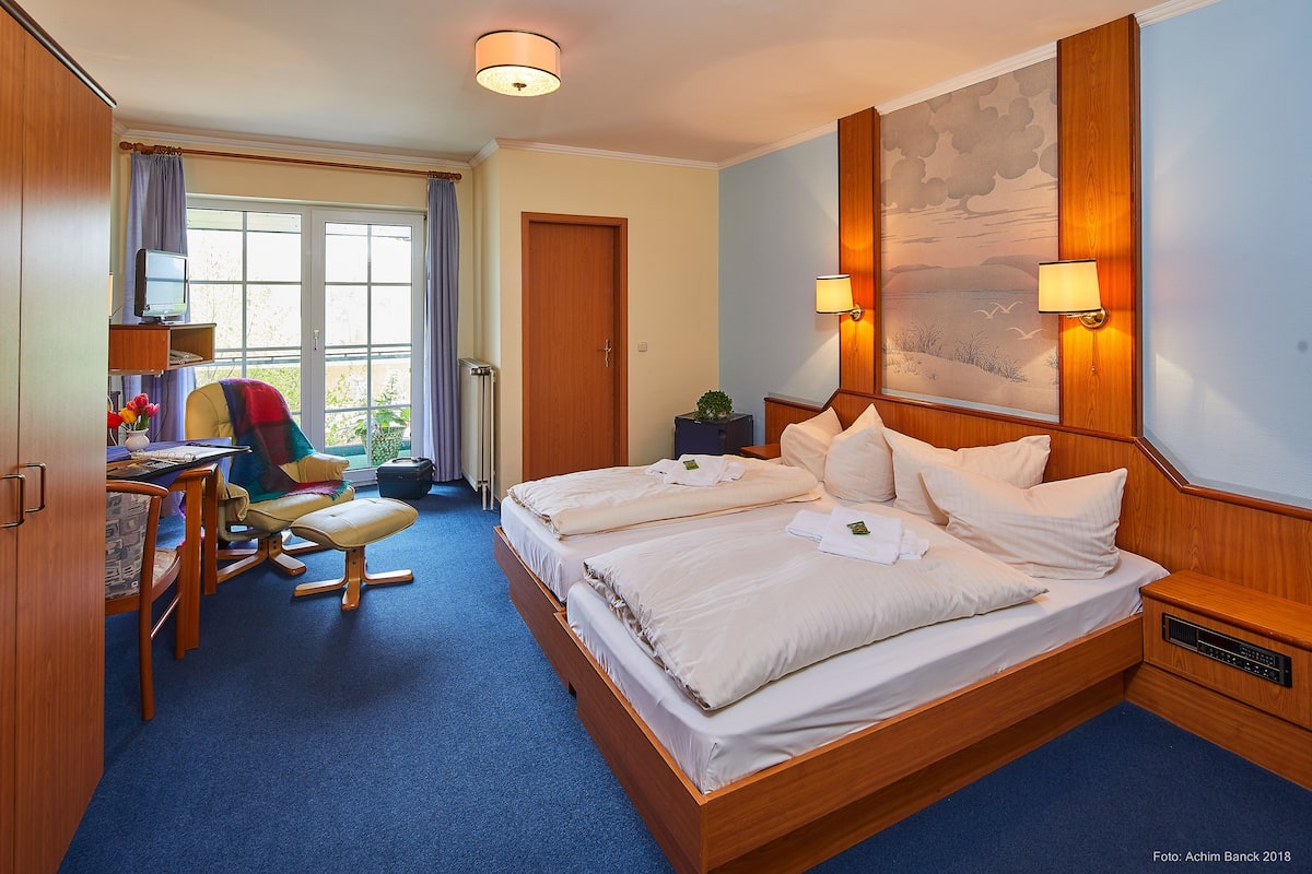 A hotel room with a large bed, a desk with a computer, and a window with curtains.