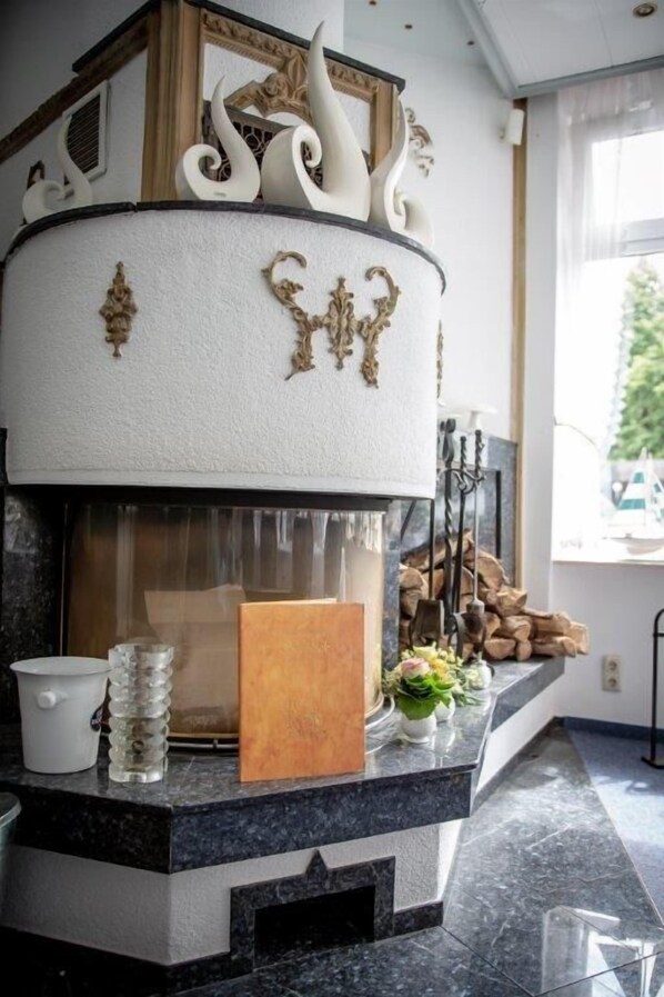 Una chimenea moderna con detalles decorativos blancos y dorados, una placa de madera y un florero con flores sobre una encimera de mármol.