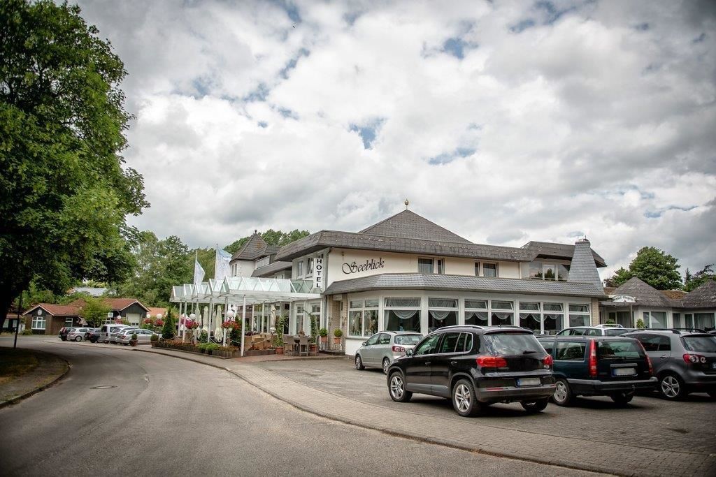 Ein Hotel mit großem Parkplatz und überdachter Außenbestuhlung.