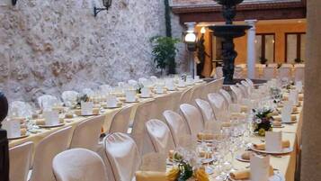 A banquet hall with long tables set for a formal event, featuring white tablecloths, glassware, and floral centerpieces.